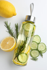 Lemon water in bottle, rosemary, fresh fruits and slices of cucumber on white background, flat lay