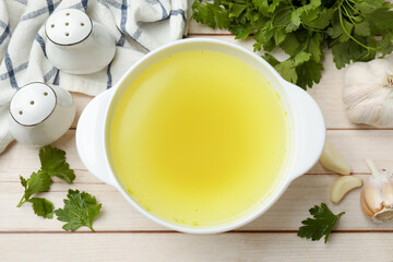 Tasty chicken bouillon in bowl and ingredients on wooden table, flat lay