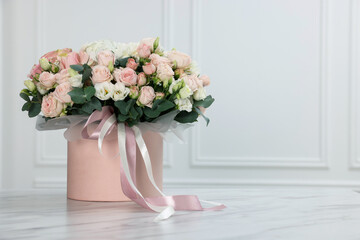 Gift box with bouquet of beautiful flowers and eucalyptus branches on marble table against white wall. Space for text