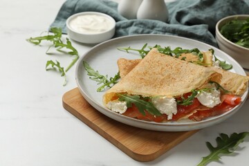 Delicious crepes with salmon, cream cheese and arugula on white table
