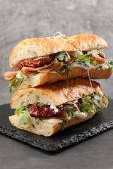 Halves of baguette sandwich with prosciutto and sun dried tomatoes on grey table, closeup