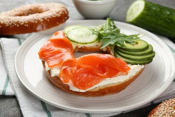 Delicious bagel with salmon, cream cheese, cucumber and avocado on table, closeup