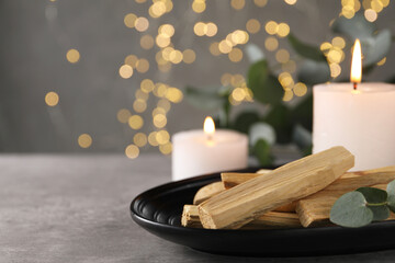 Palo santo sticks, eucalyptus branch and burning candles on grey table, closeup. Space for text