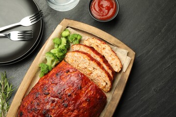 Delicious turkey meatloaf with vegetables served on black table, flat lay