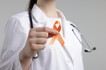 Multiple Sclerosis awareness. Doctor holding orange ribbon on light grey background, closeup