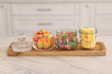 Tasty gummy candies in glass jars on white marble table