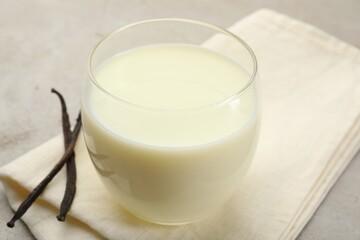 Glass of milk and vanilla pods on light grey table, closeup