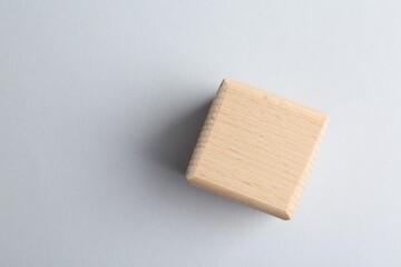 One wooden cube on light grey background, top view. Space for text