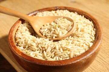 Brown rice and spoon in bowl on wooden table, closeup