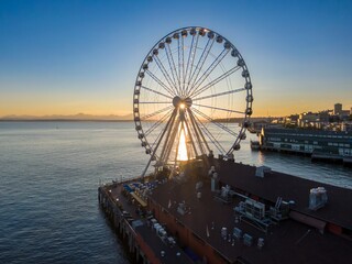 Sunset view of the Seattle Great Wheel over Puget Sound. Golden light illuminates the Ferris wheel,...