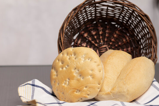 un par de panes, una marraqueta, una hallulla que salen de un canasto sobre un pa&ntilde;o de cocina blanco