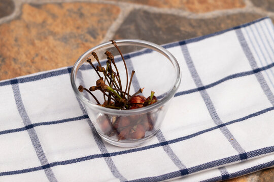 palos y cuescos de guindas en un vaso de vidrio sobre un pa&ntilde;o de cocina