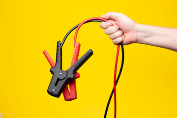 Jumper cables with clamps held in hand yellow background.

