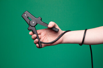 Hand holding car jumper cable. Green background, studio, no face. 
