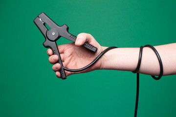 Jumper cables firmly held by a man's hand, photographed in a studio with a green backdrop. Minimalist composition, no face shown. 
