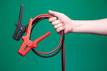 Man holding jumper cables in hand against a green studio background. Close-up shot, no face visible, with copy space. 
