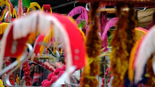 The background showcases vibrant, colorful decorations with intricate designs, evoking a festive, cultural, and traditional atmosphere, possibly part of a religious or ceremonial celebration.