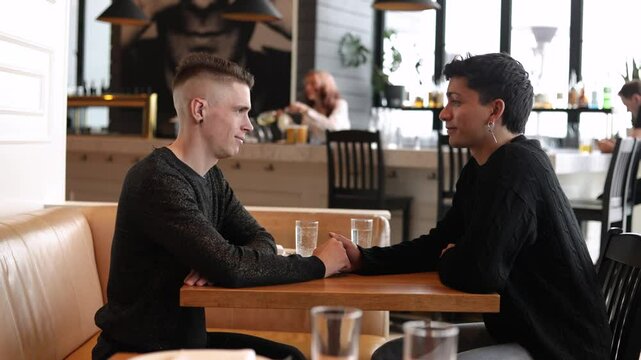 A medium shot of a gay men couple on a date in a cozy cafe
A mid shot of a LGBTQ+ couple on a romantic date, a man timidly touching his partner's hand and kissing him across a table in an urban cafe
