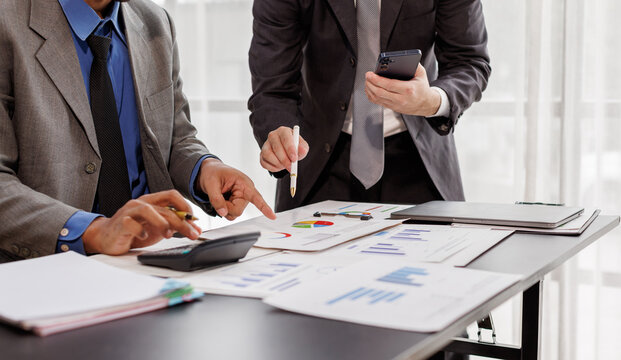 Team of confident business people point to graphs and smartphone use charts to analyze market data, balance sheet, account, net profit to plan new sales strategies to increase production capacity.
