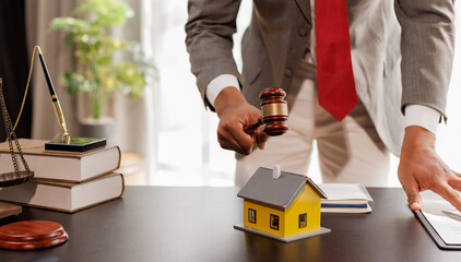 Real Estate Law, Home Insurance, property Tax, Auction and Bidding concepts. small toy house model with gavel justice hammer on desk in courthouse.
