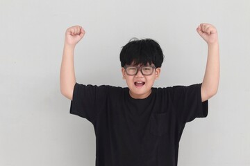 Asian boy celebrating success with raised fists. His joyful expression shows motivation and pride....
