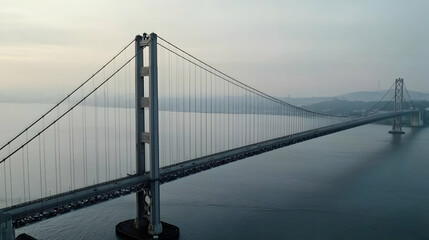 Fototapeta premium Elevated View of Suspension Bridge Over Calm Water in a Cityscape Under Cloudy Sky