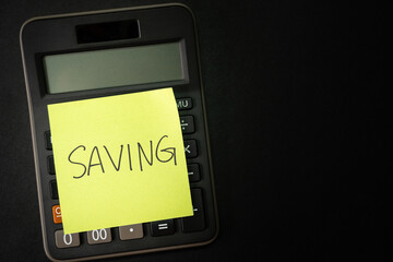 Fototapeta premium SAVING text with sticky note on calculator. financial concept. Saving money concept. Retirement concept. Pension calculation concept. Copy space.