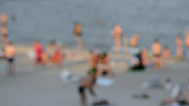 Lots of people on beach by sea on summer evening. Many men and women in bathing suits and swimming trunks on sandy beach on seashore. Rest and relaxation on beach. People sunbathing Blurred background