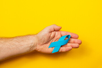 Hand holding a blue ribbon symbolizing cancer awareness and support