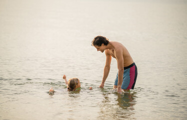 Father and child enjoying a warm summer day while playing in the calm water at the beach during sunset