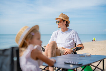 Fototapeta premium Father and daughter enjoy a relaxing day at the beach with sun hats and chairs