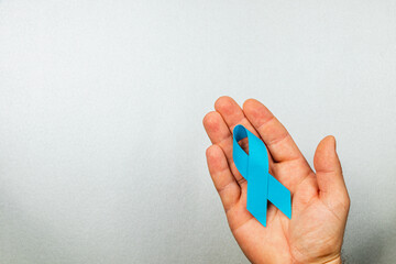 Hand holding a blue ribbon symbolizing awareness for cancer prevention