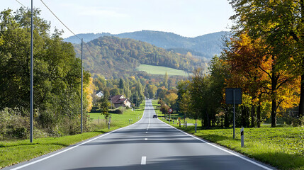 Long Straight Road Through Autumn Landscape With Trees And Mountains Under Blue Sky