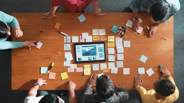 Top down view of programmer brainstorming and planning about web design while looking at tablet wireframe prototype. Aerial view of skilled developer team talking about digital application. Symposium.