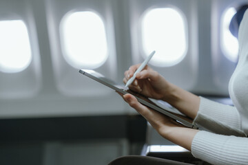 A businesswoman is sitting at the airplane window typing on her laptop while traveling. She is focused and relaxed. She is able to balance work and leisure, which is a symbol of independence.
