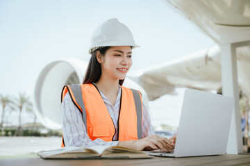 Professional female aerospace engineer wearing hard hat inspects aircraft engine, holding tablet and blueprints to ensure precision and safety in aircraft maintenance, symbolizing expertise and innova