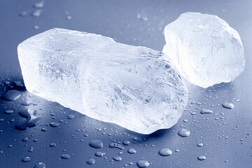 Pieces of clear ice and water drops on light blue table, closeup