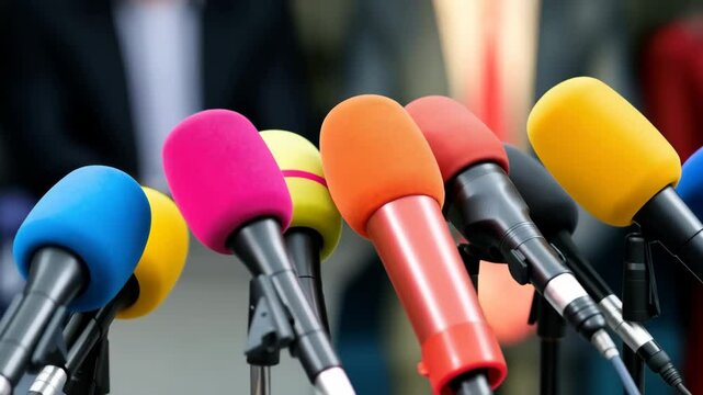 Group of colorful microphones arranged in a row on a metal stand. The microphones are of different colors - blue, pink, orange, yellow, and red.