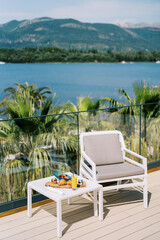 Continental breakfast stands on a table near an armchair on the hotel terrace by the sea