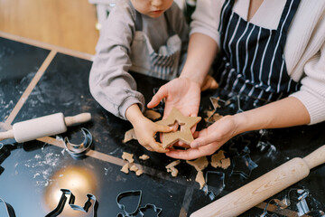 Little girl touches a cut-out cookie in her mother palm with her finger. Cropped