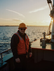 Male worker in safety gear on sea vessel during sunset