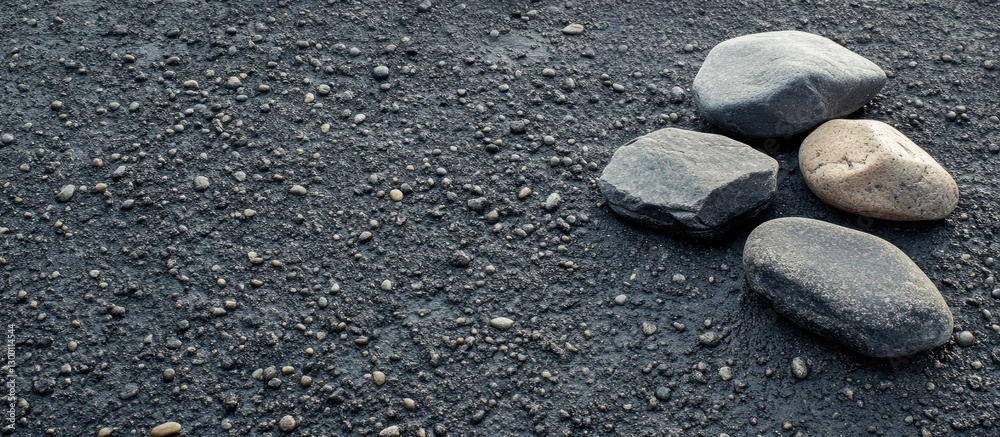 Poster natural gray and beige stones arranged asymmetrically on a textured dark asphalt surface, creating a