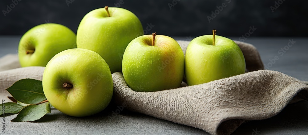 Aufkleber fresh green apples arranged elegantly on a soft gray cloth with green leaves, set against a dark tex