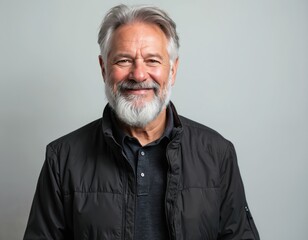 Obraz premium Happy mature man portrait with beard, gray hair smiling on grey background. Bearded senior male looks at camera with cheerful smile, good mood. Confident middle aged person wears casual attire.