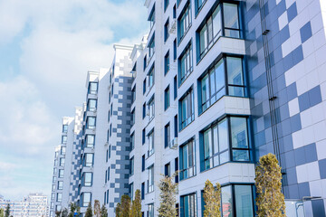 Side view of a multi-storey residential building of modern architecture with large windows against the background of the sky with clouds, the house is lined with white and gray slabs. The concept of