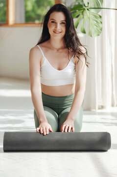 Portrait of cute lady sitting on floor and rolling yoga mat