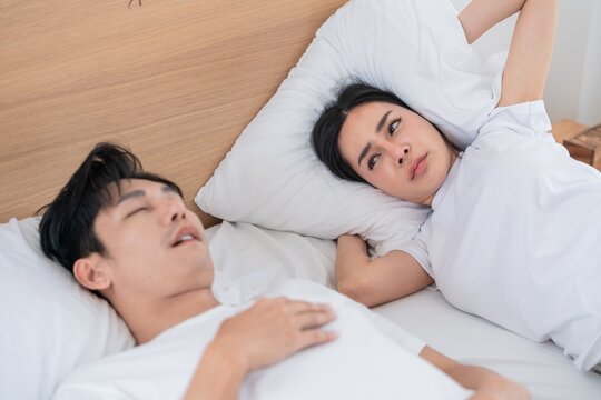 Couple in bed with one partner snoring, causing disruption at morning in a cozy bedroom setting