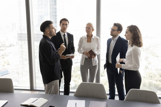Equality in partnership. Corporate employees group diverse age gender meet for talk by panoramic window in office conference room listen to colleague hipster offering creative idea innovative approach