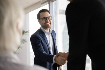 Success in negotiation. Smiling confident young businessman in formal suit handshake make deal with partner on stakeholders group meeting. Happy job seeker shake employers hand getting job. Copy space