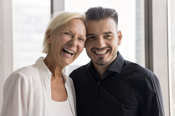 Diversity and bonds of friendship. Head shot portrait happy smiling older age elegant woman mentor young hipster man intern having bonding warm relationship hug smile look at camera at corporate event